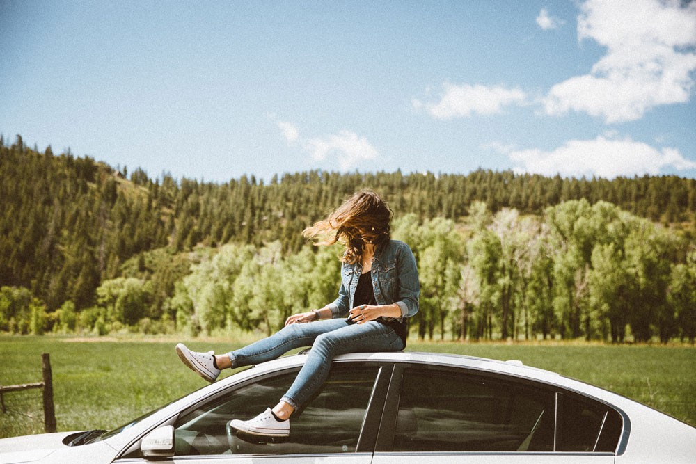 chica joven subida en un coche con el pelo al viento y detrás montañas